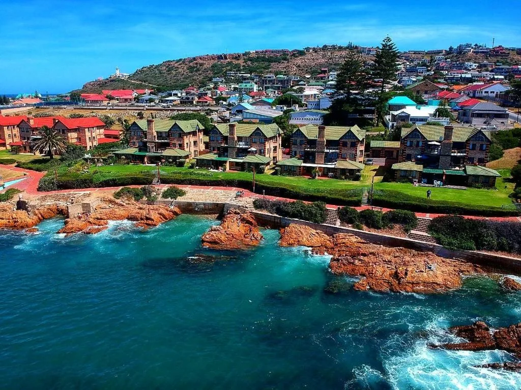 Turquoise ocean, red rocky cliffs, beachfront properties with green roofs