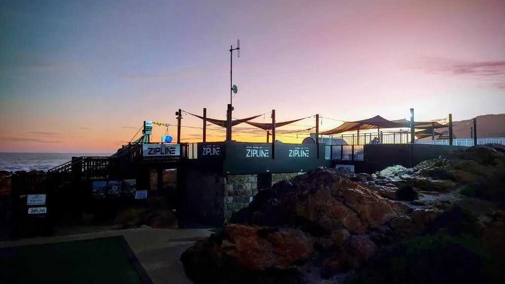 Sunset over ocean with zipline adventure platform and rocky coastline