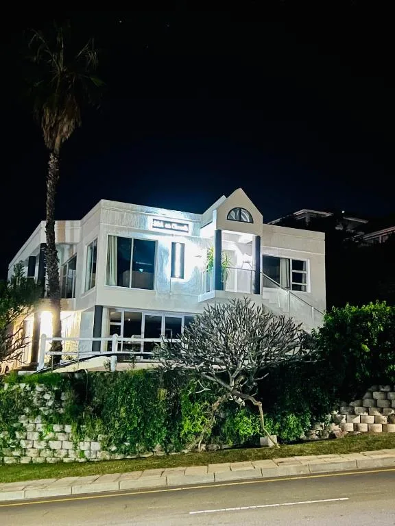 Modern white beachfront house illuminated at night with palm tree and landscaping