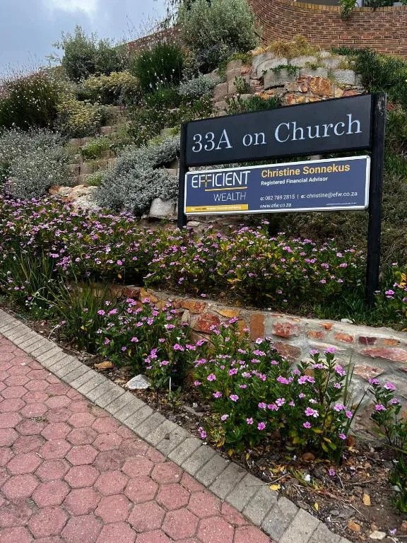 Property entrance sign with vibrant purple flowers and stone wall landscaping