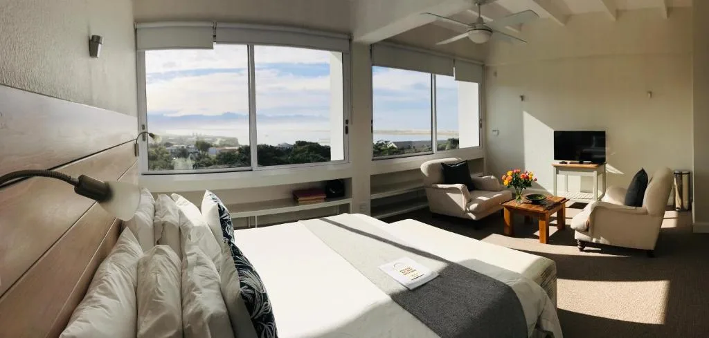 Bright bedroom with bed, lounge area, and expansive mountain views through windows