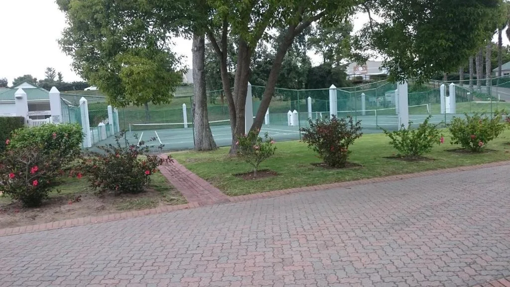 Manicured garden with flowering shrubs, mature tree, and white fence bordering tennis courts