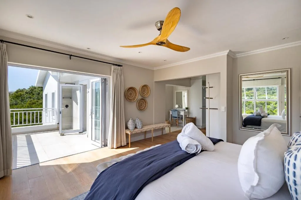 Spacious bedroom with king bed, wooden ceiling fan, and deck access