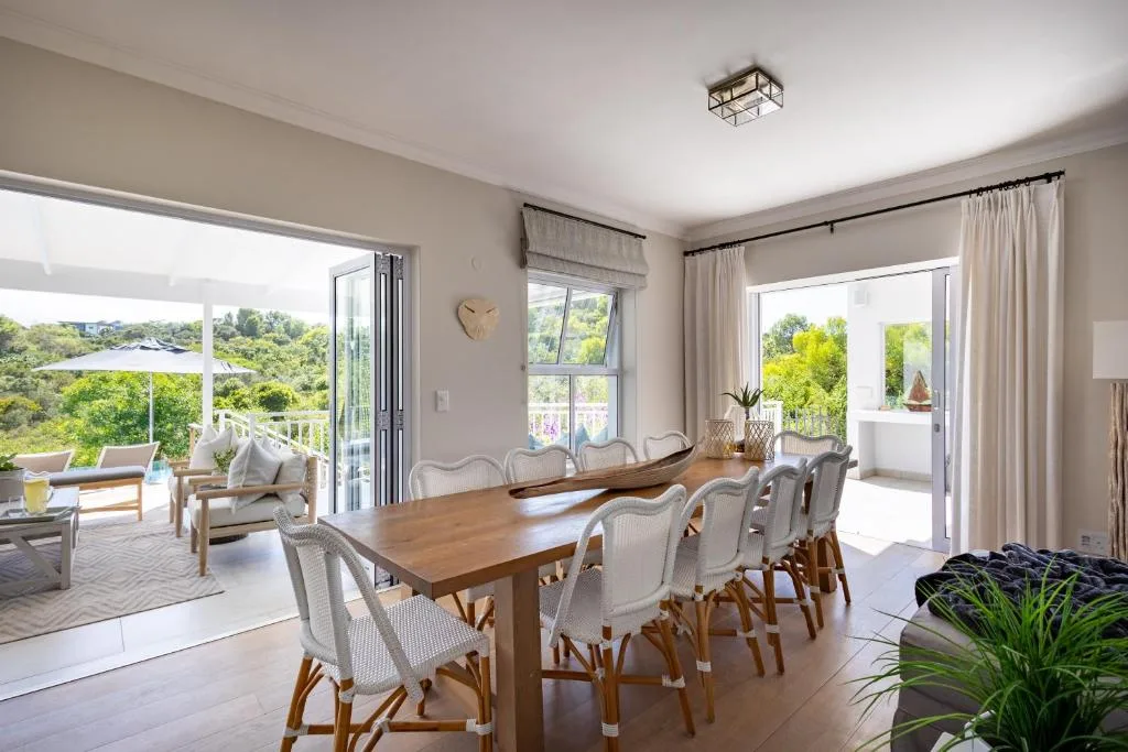Spacious dining room with wooden table and cream upholstered chairs, opening to scenic garden views