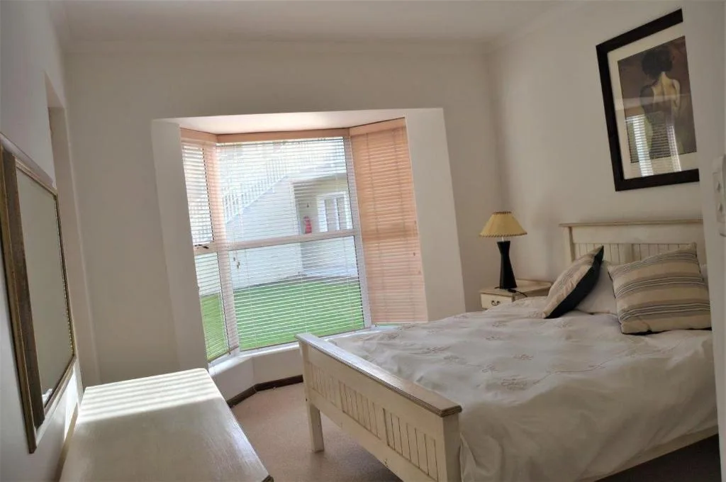 Bright bedroom with white bed, bedside lamp, and garden view through large windows