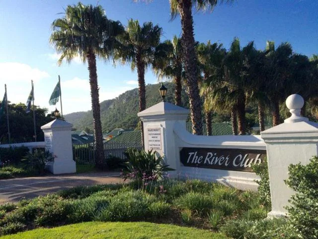 The River Club entrance with white pillars, palm trees and mountains