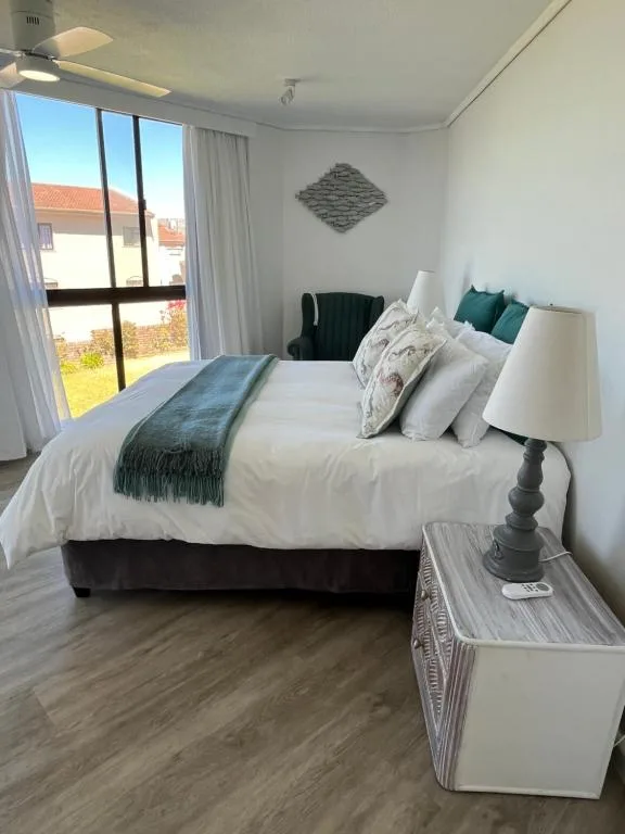Bright bedroom with queen bed, white bedding, teal accents, and garden views