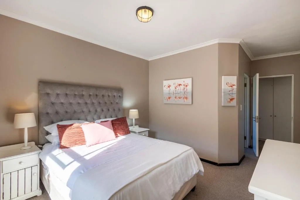Spacious bedroom with tufted headboard, white bedding, and flamingo artwork