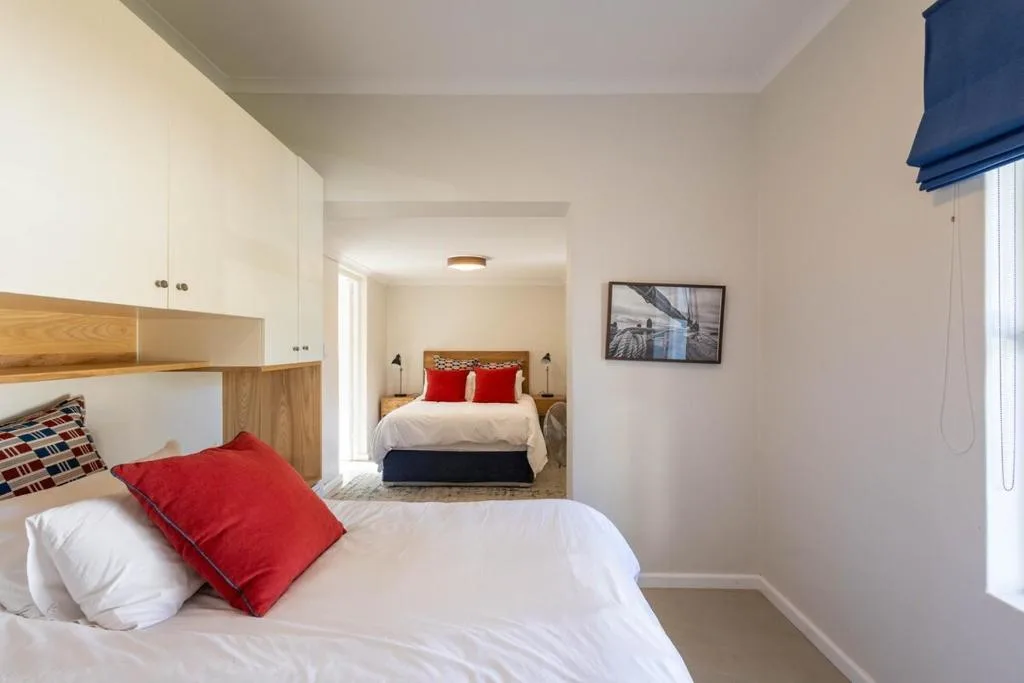 Modern bedroom with white bedding, red accent pillow, and adjoining ensuite area