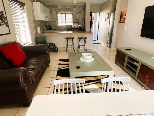 Open-plan living area with brown leather sofa, TV unit, and kitchen visible