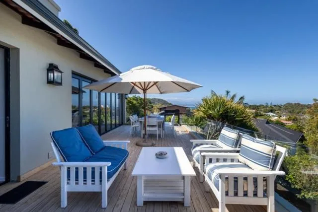 Spacious wooden deck with white furniture, umbrella, and mountain views