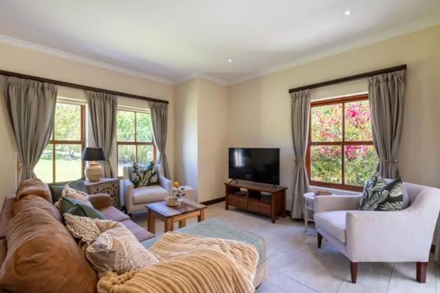 Bright living room with sofa, armchairs, TV, and garden views through windows