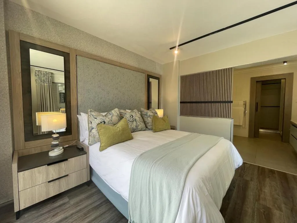 Modern bedroom with queen bed, patterned cushions, and wooden vanity mirror