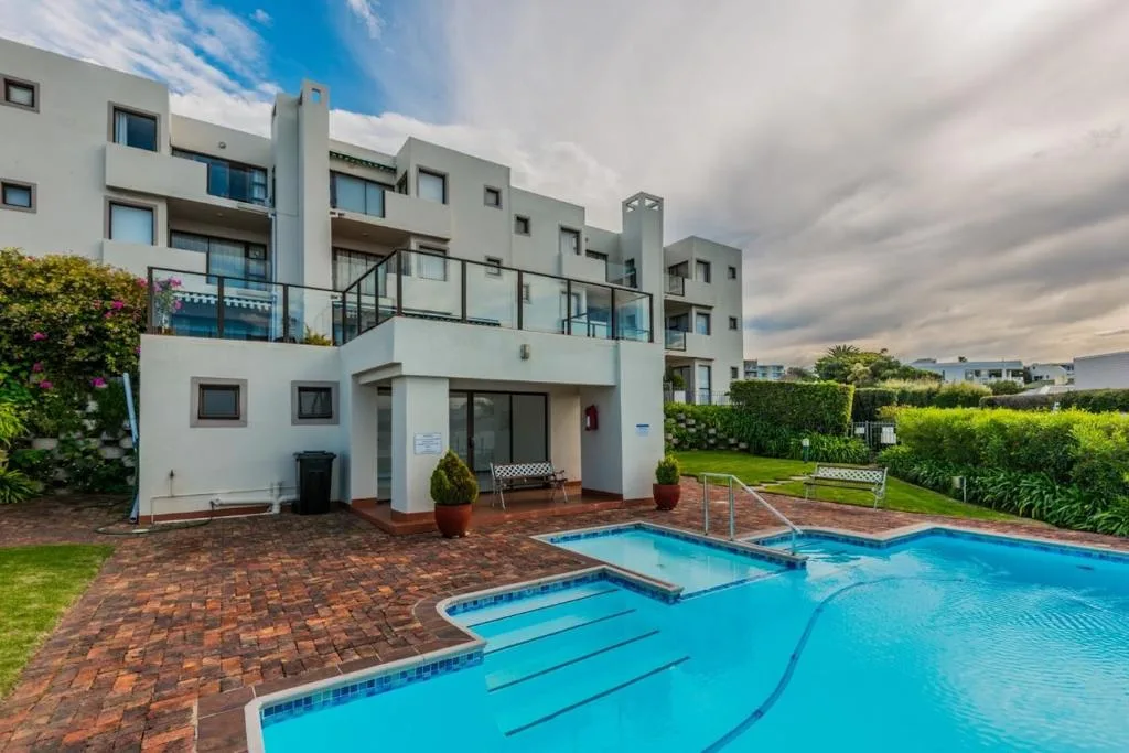 Bright blue swimming pool with loungers in front of modern white apartment building