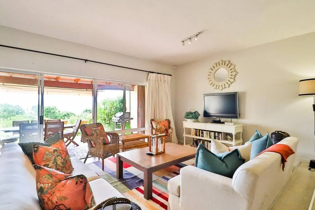Spacious lounge with cream sofa, orange patterned chairs, TV, and deck access