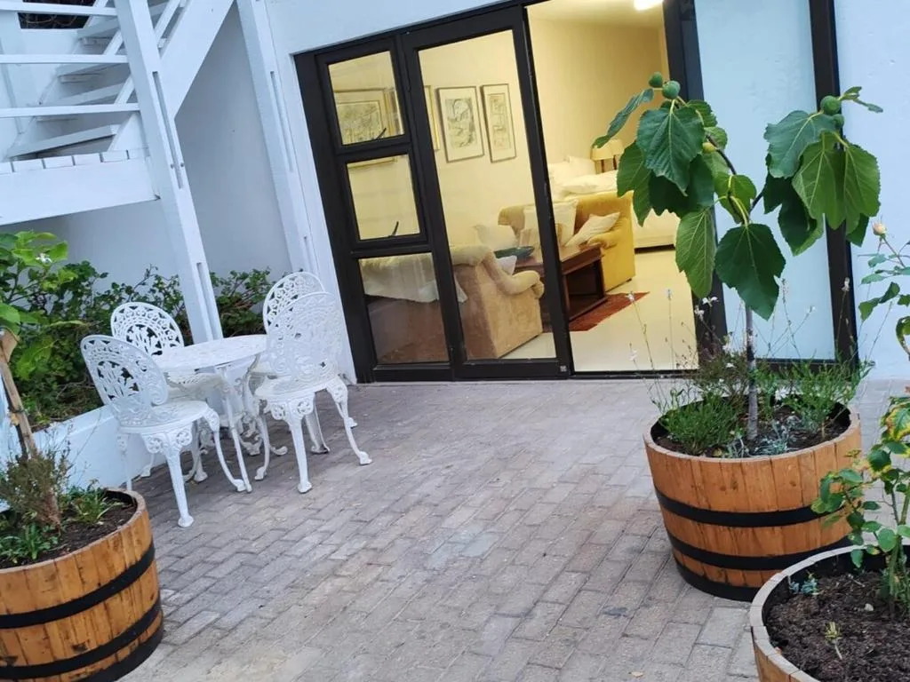 Paved patio with white chairs and potted plants beside interior