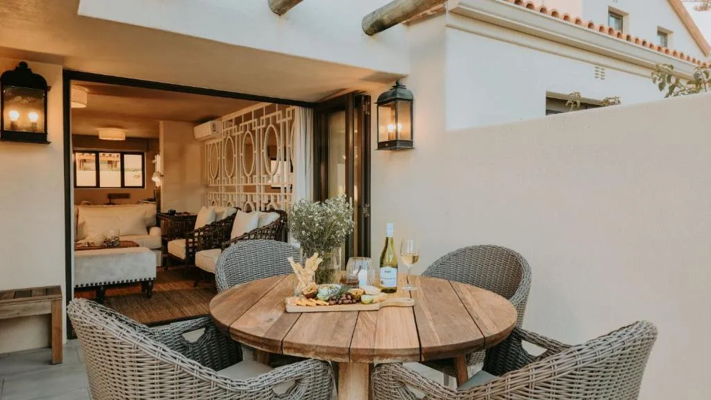 Outdoor patio with round wooden table and wicker chairs overlooking bedroom