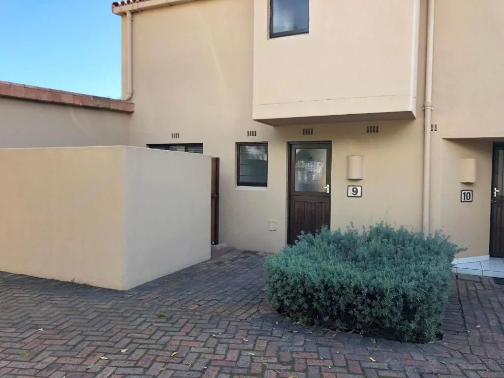 Cream-colored townhouse unit nine with dark wooden door and landscaping