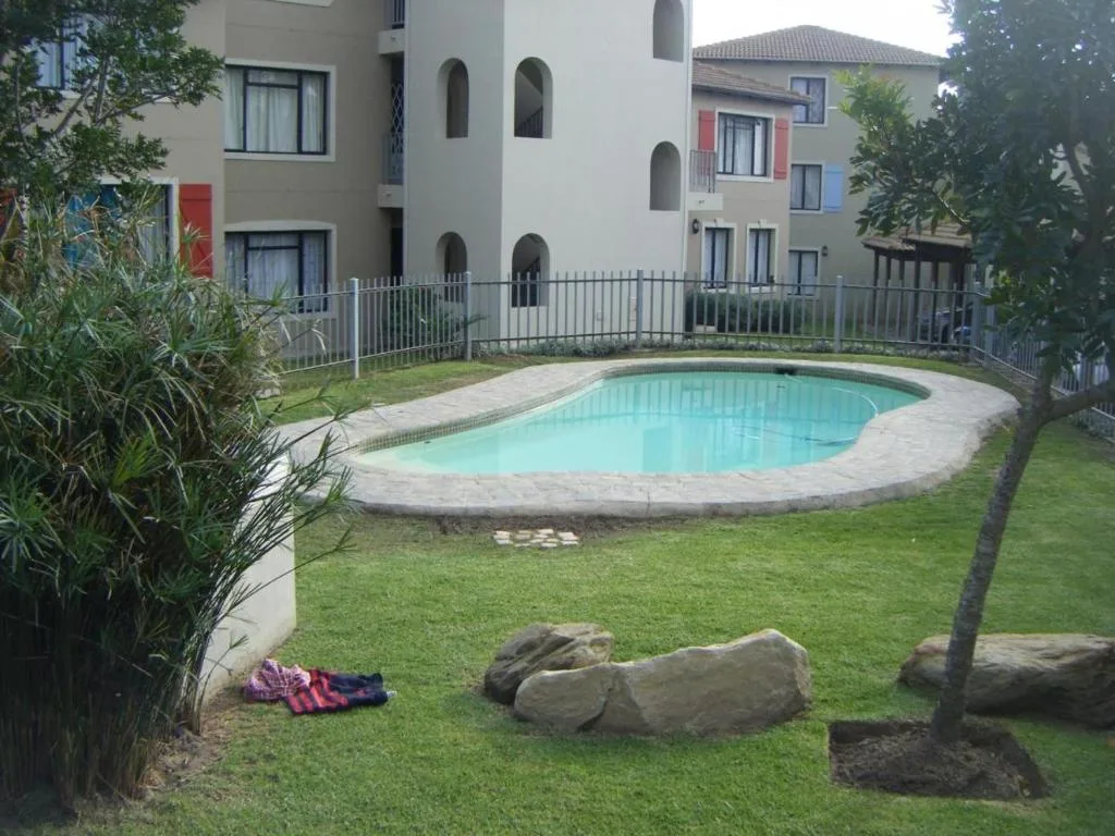 Turquoise swimming pool surrounded by manicured lawn and modern apartment buildings
