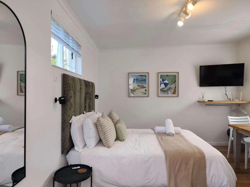 Bright bedroom with upholstered headboard, white linens, and wall-mounted TV