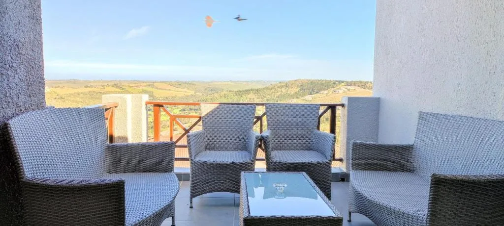 Outdoor seating area with rattan chairs overlooking lush valley landscape