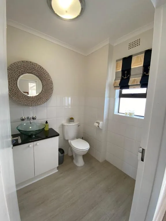 Modern bathroom with glass basin sink, toilet, and decorative round mirror