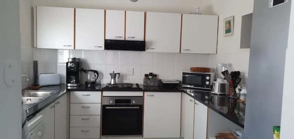 Compact kitchen with white cabinetry, black countertops, and integrated appliances