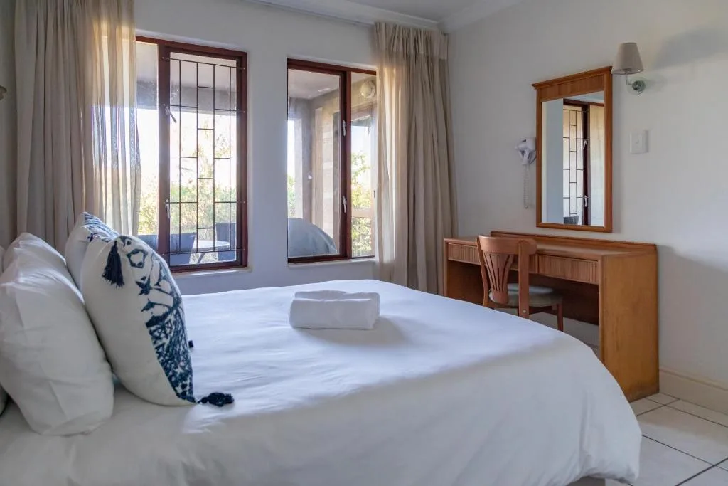 Bright bedroom with queen bed, wooden vanity, and garden views through French doors