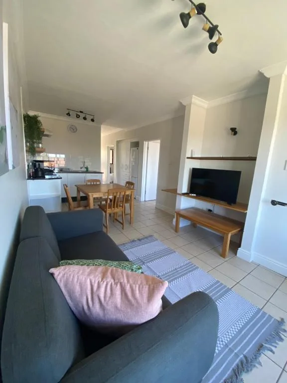 Open-plan lounge with dark sofa, TV stand, and kitchen visible beyond