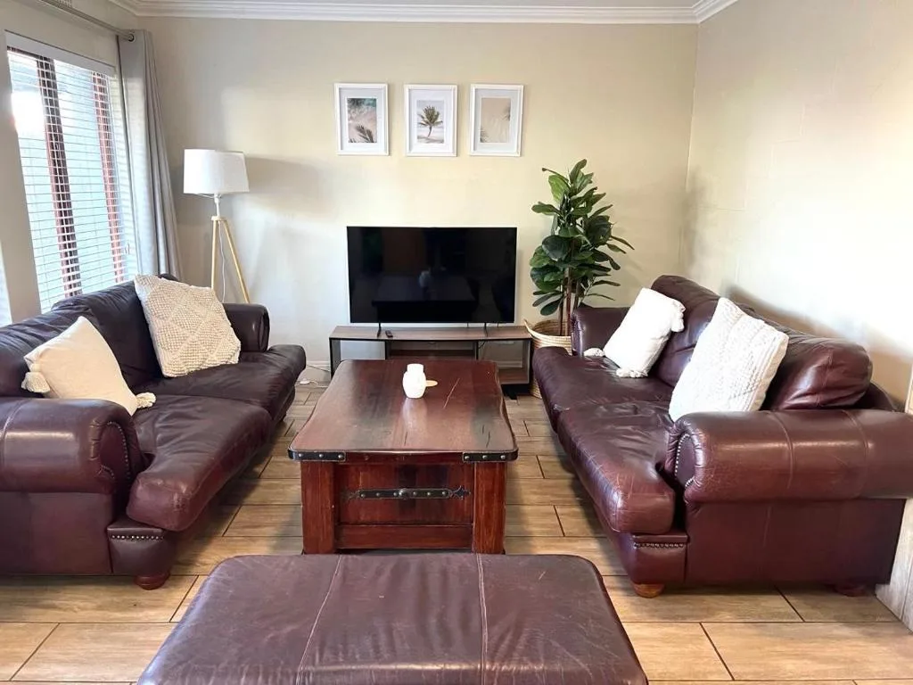 Spacious living room with brown leather sofas, TV, and potted plant