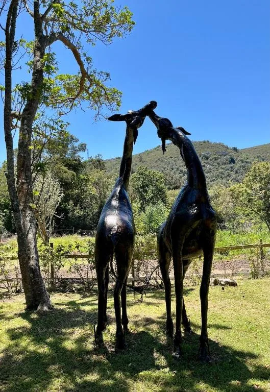 Black metal giraffe sculpture in lush garden with hillside backdrop
