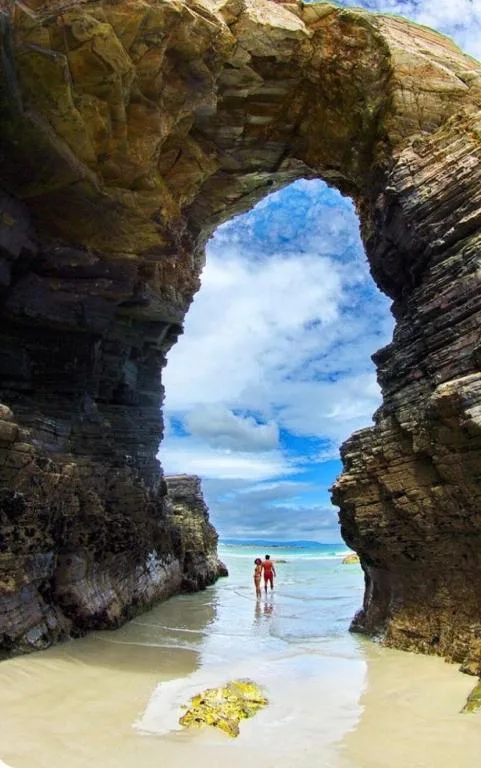 Scenic coastal rock arch framing ocean and beach with two people wading