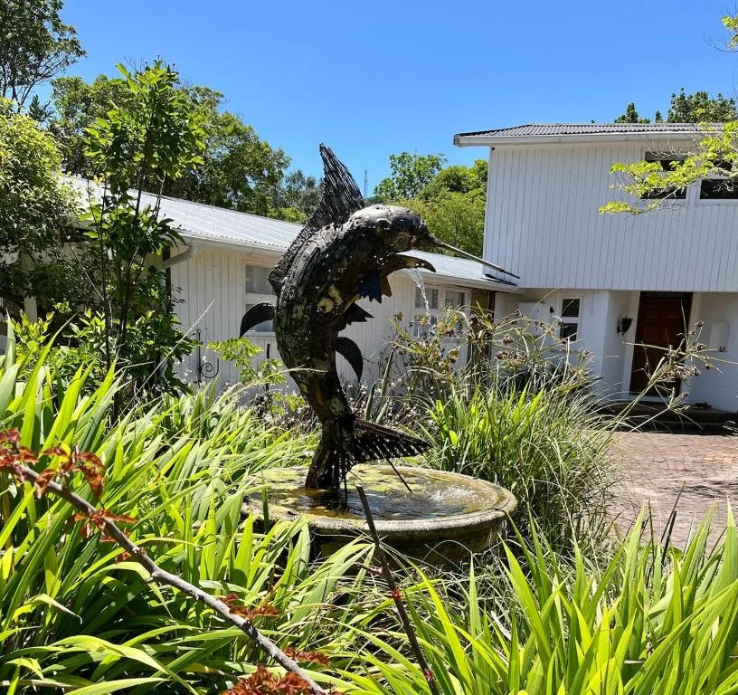 Modern white cottage with fish sculpture and lush garden landscaping