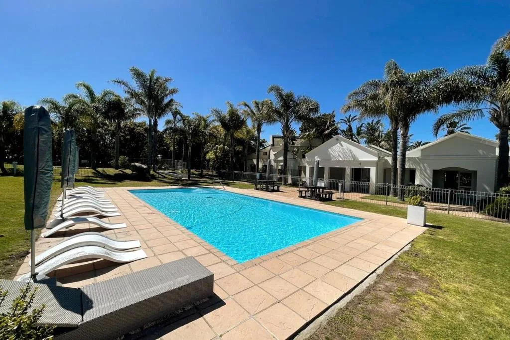 Resort swimming pool with loungers, white buildings, and palm trees