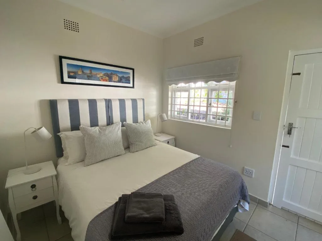 Bright bedroom with striped headboard, white bedding, and window overlooking town