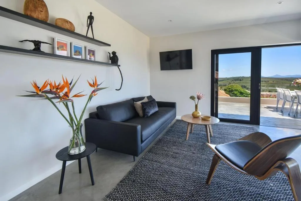 Modern lounge with black sofa, armchair, and scenic garden route views through glass doors