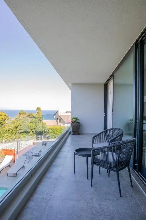 Modern balcony with seating overlooking ocean and coastal vegetation