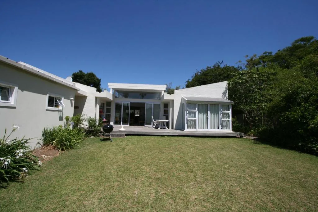 Modern white holiday home with manicured lawn and lush garden surroundings