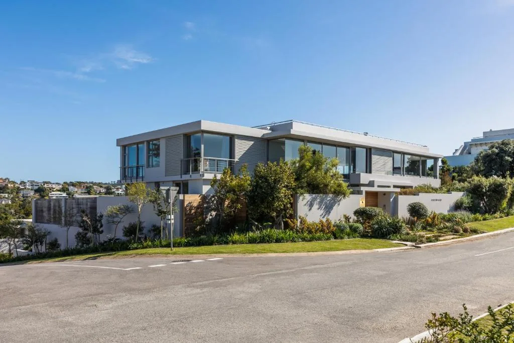 Modern two-story villa with white facade and large windows, surrounded by manicured gardens