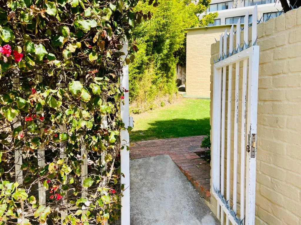 Garden entrance with flowering vines and white gate leading to lawn