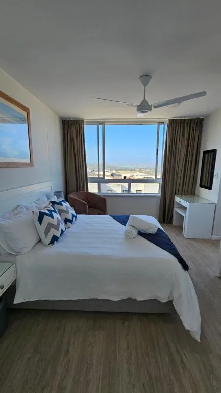 Bright bedroom with queen bed, expansive windows overlooking coastal landscape, ceiling fan