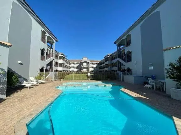 Bright turquoise swimming pool surrounded by apartment buildings and wooden deck