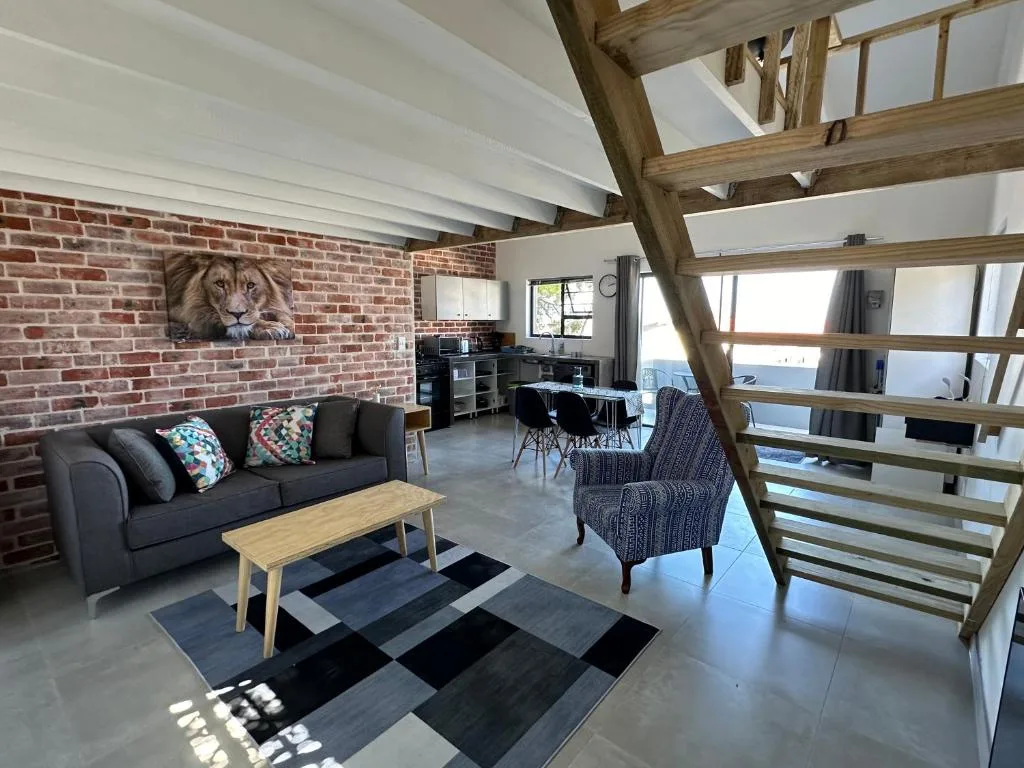 Open-plan lounge with exposed brick wall, dark sofa, wooden beams, and ocean views