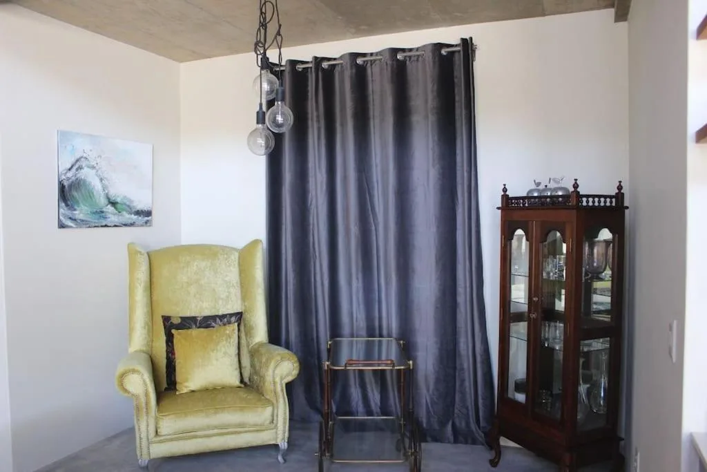 Bedroom with yellow wingback chair, dark curtains, wooden cabinet, and artwork