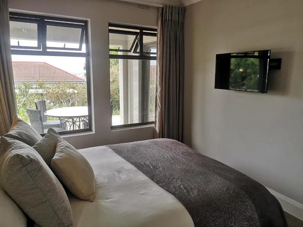 Modern bedroom with queen bed, wall-mounted TV, and garden views through large windows