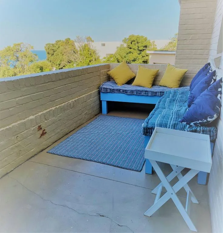 Rooftop deck with blue bench seating, yellow cushions, ocean view glimpse beyond