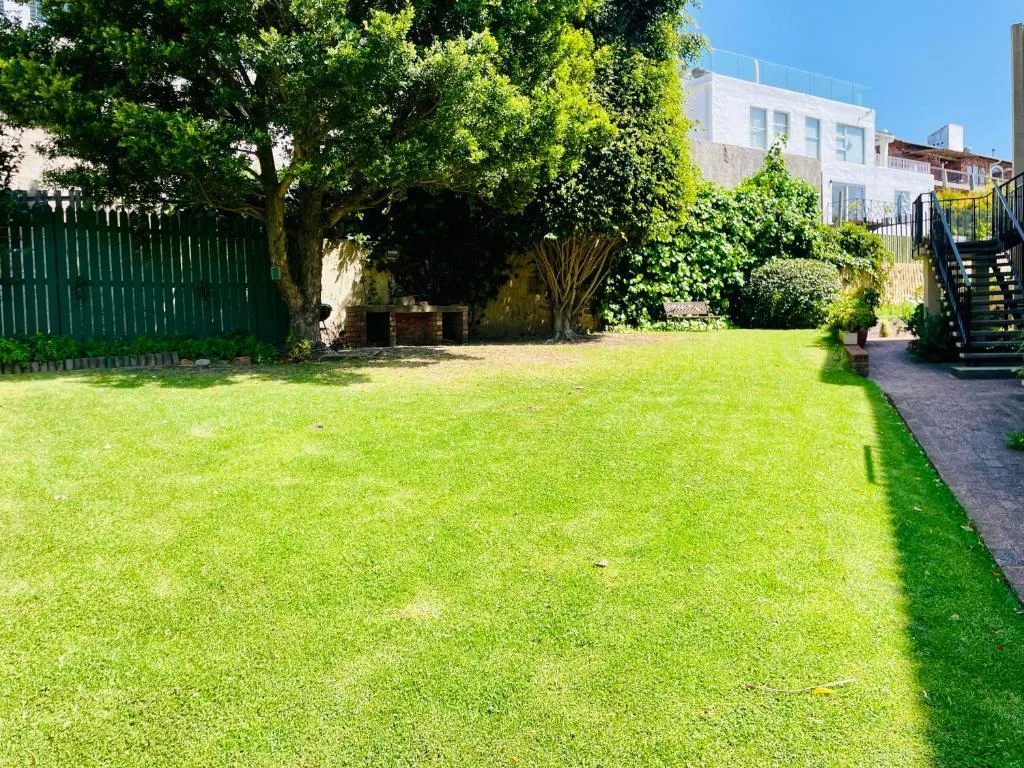 Lush green garden with mature trees and white building in background