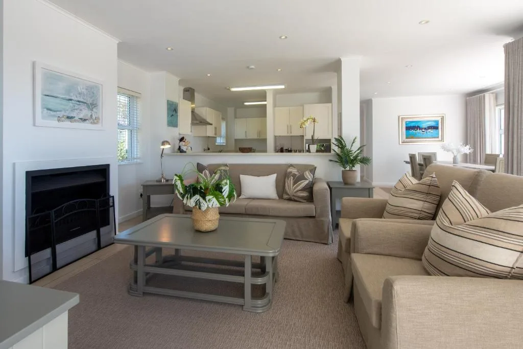 Open-plan lounge with neutral sofas, fireplace, and kitchen visible beyond