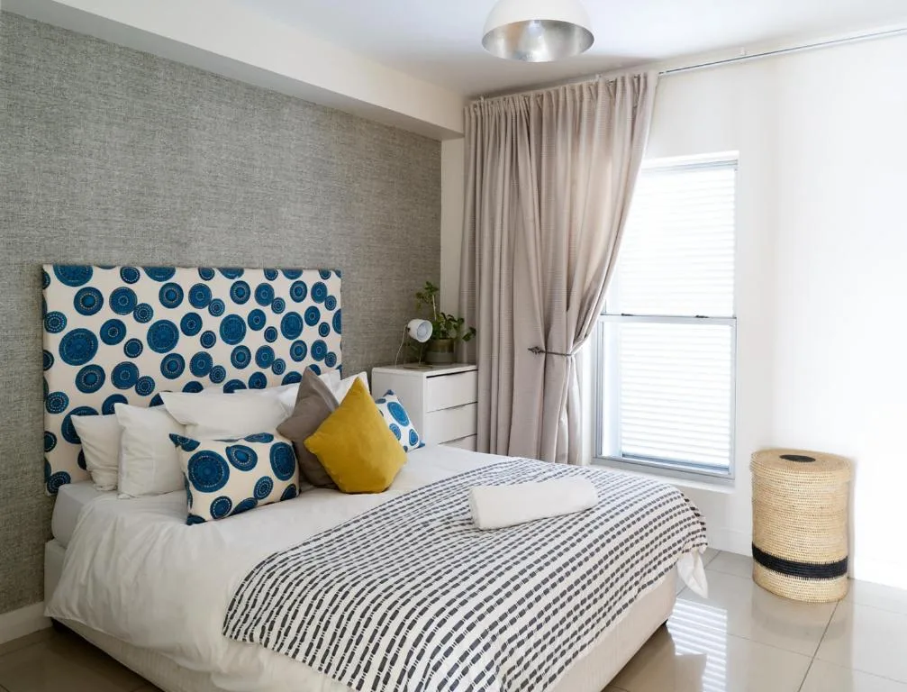 Modern bedroom with patterned headboard, white bedding, and yellow accent pillow