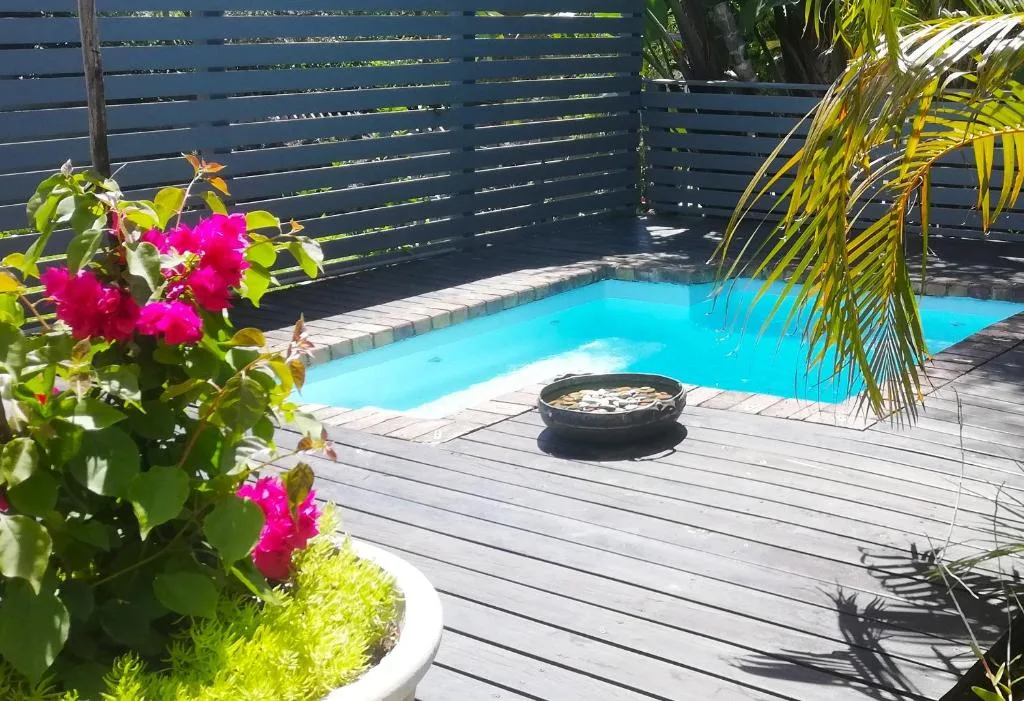 Turquoise swimming pool with wooden deck, fire pit, and tropical garden flowers